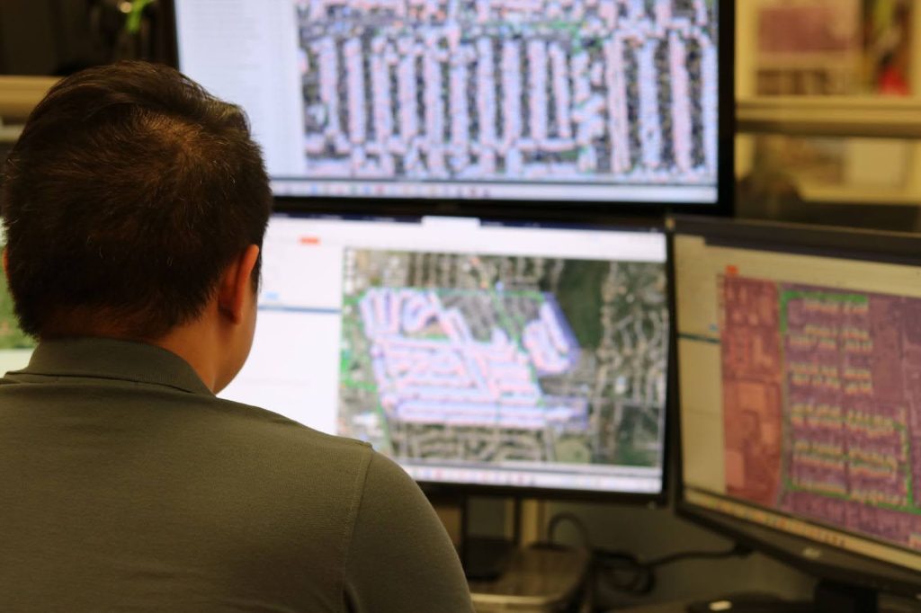  A professional analyzing maps on multiple screens for GPS-tracked door hanger distribution, ensuring precise and targeted delivery.